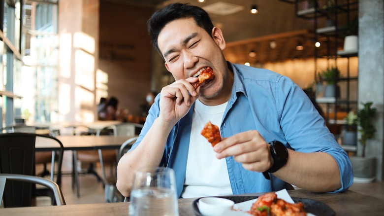 Happy,asian,man,eating,bbq,chicken,wings,in,restaurant.